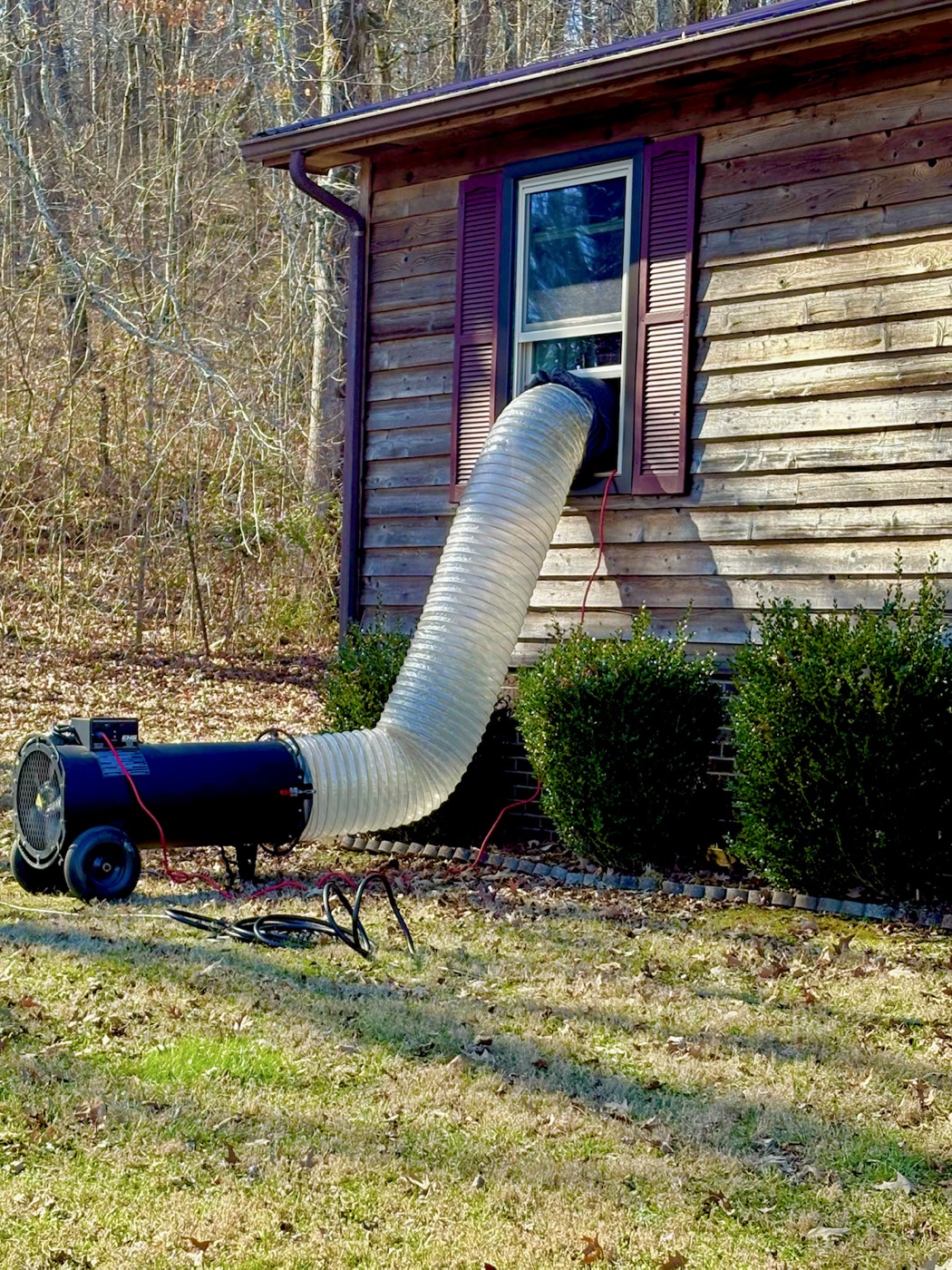 EcoForce heat treatment hose entering a side window of a wood-sided house